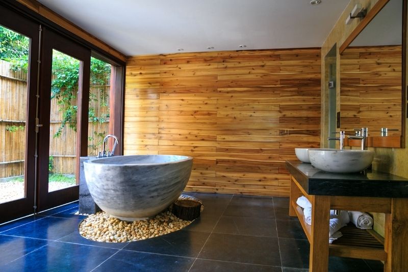 Timber-lined bathroom with a stone freestanding bath and double vessel sinks opening to a courtyard