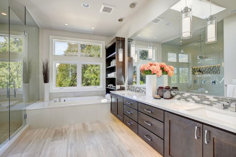 Spacious ensuite with a dark timber vanity, freestanding bath and glass shower framed by large windows