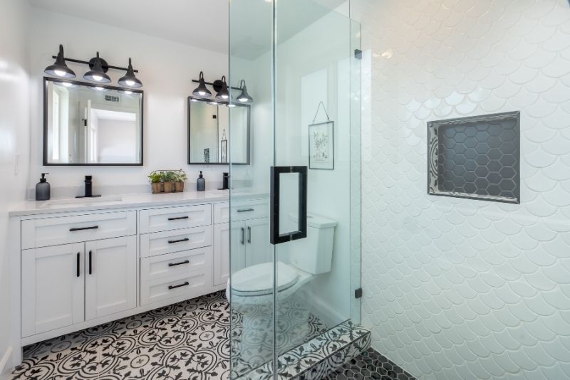 Modern black-and-white bathroom with a heated towel rail, double vanity, patterned tile floor and glass-enclosed scallop-tile shower