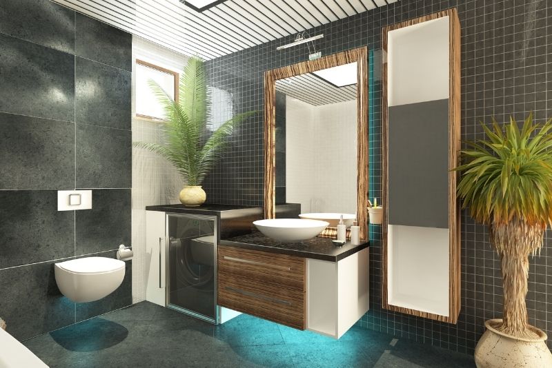Dark-tiled bathroom with a wall-hung toilet, timber-framed mirror and built-in laundry cabinetry