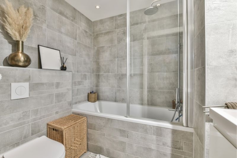 Grey-tiled bathroom with a glass shower-over-bath and patterned tile flooring