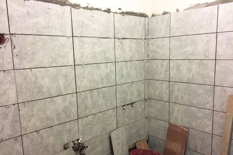Bathroom shower wall mid-renovation with newly installed grey tiles and exposed plumbing