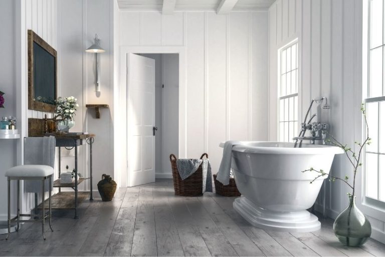 Freestanding bath in a white panelled bathroom with timber flooring and large windows